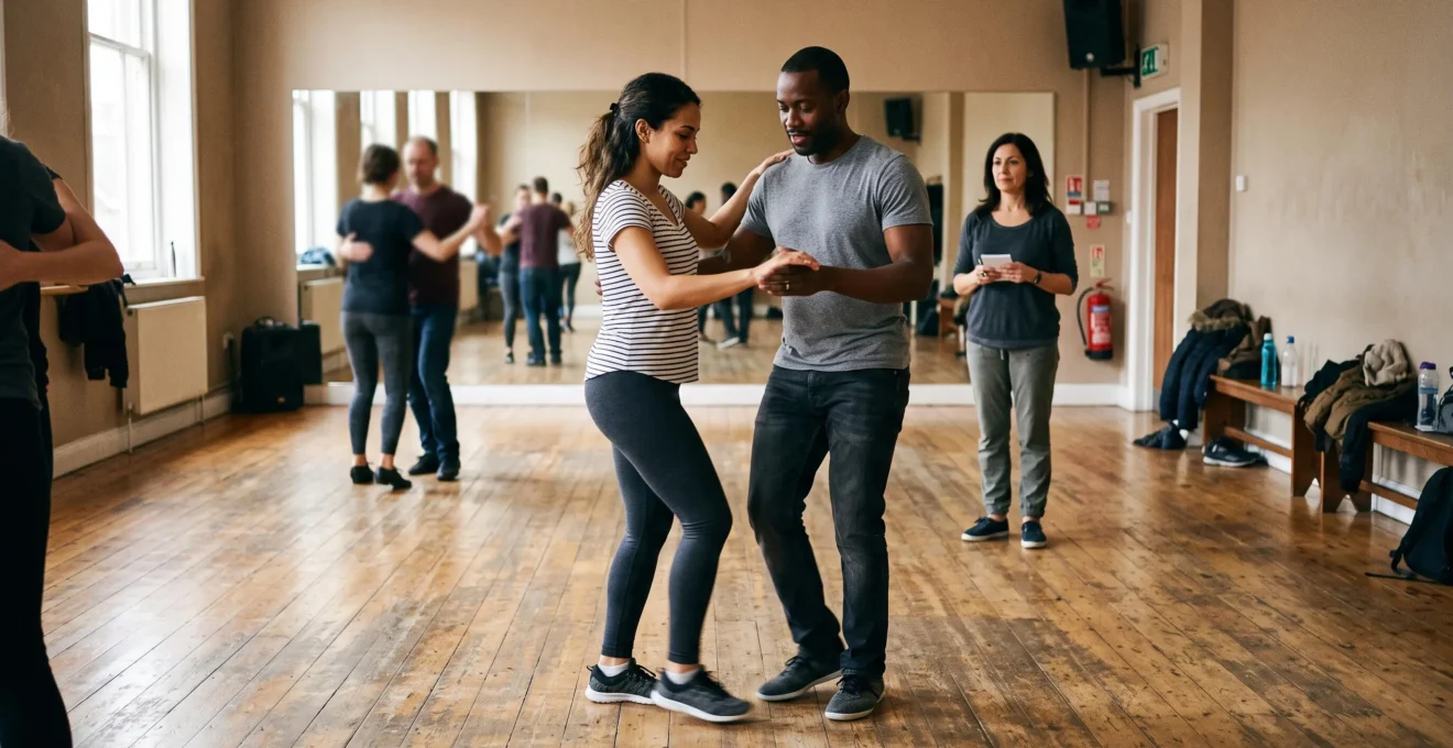 Un couple débutant danse le pas de base de bachata dans un studio, transférant le poids avec les genoux souples et le bassin relâché, tandis que le professeur observe en retrait.
